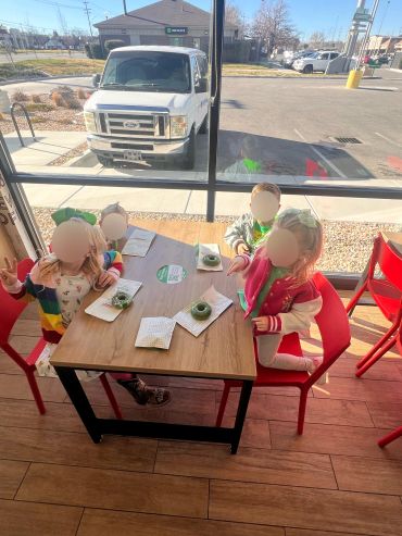 Four children sitting around a table in a cafe with green donuts.