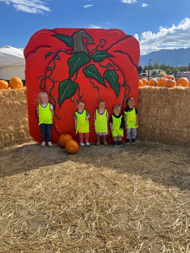 Kids in neon vests at pumpkin patch with large pumpkin mural.