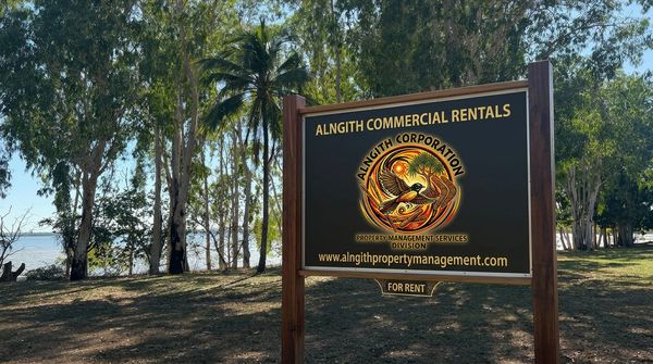 Signboard for Alngith Commercial Rentals in a wooded area near water.