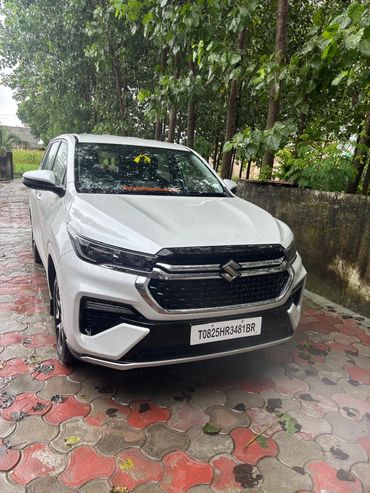 White Suzuki car parked on a wet tiled driveway near trees.