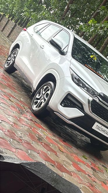 White Suzuki SUV parked on wet pavement with umbrella in foreground.
