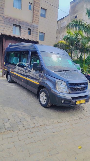 A grey tourist van parked on a paved area near buildings and palm trees.