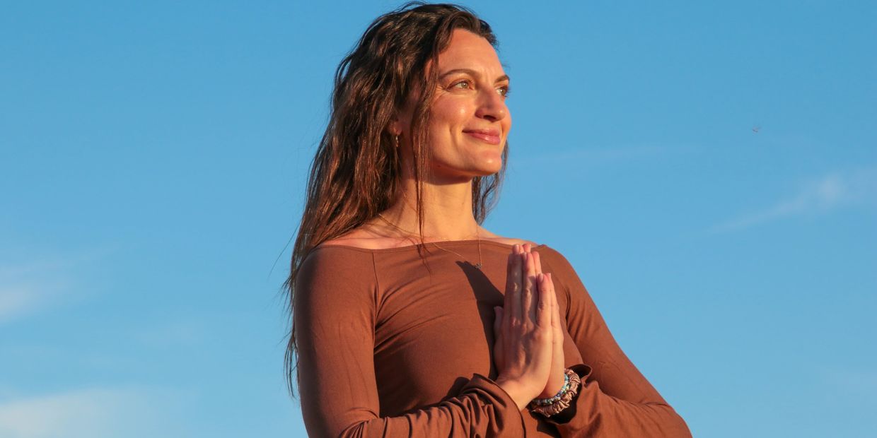 Woman practicing meditation with hands in prayer under blue sky.