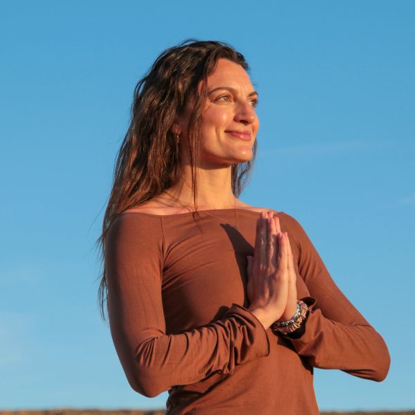 Woman practicing meditation with hands in prayer under blue sky.