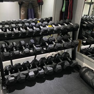 A rack filled with various sizes of black hex dumbbells in a gym.