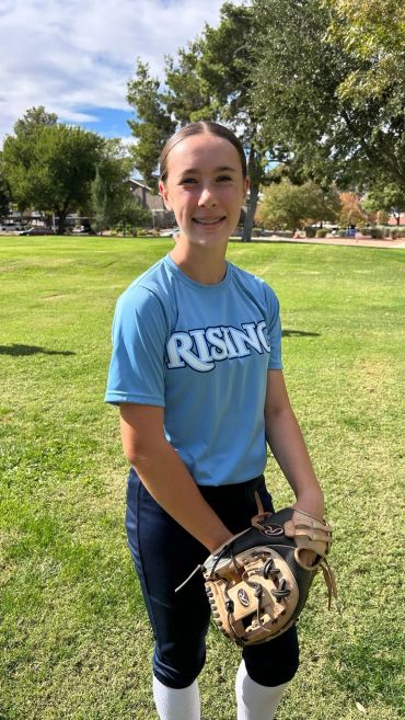 A young softball player in uniform holding a glove on a grassy field.