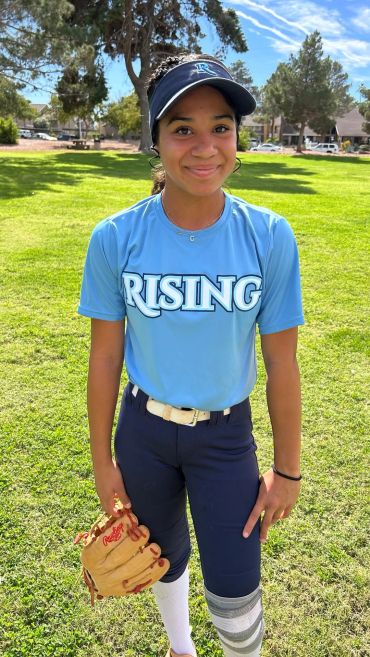 Young softball player in blue Rising jersey smiling outdoors.
