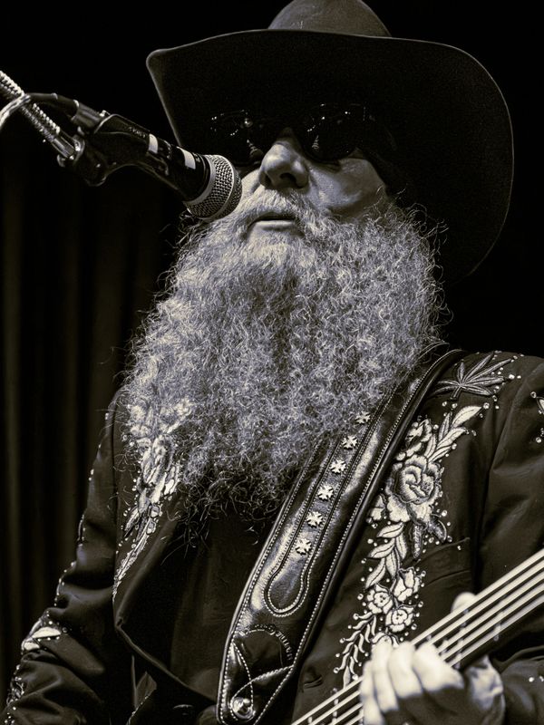 Bearded musician with sunglasses and cowboy hat performing on stage.