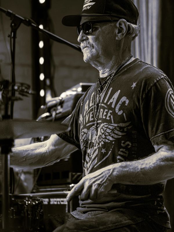 Elderly man playing drums with focus and intensity in a casual setting.