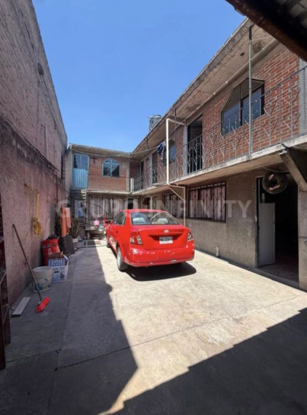 Patio con un coche rojo estacionado y edificio de dos pisos.