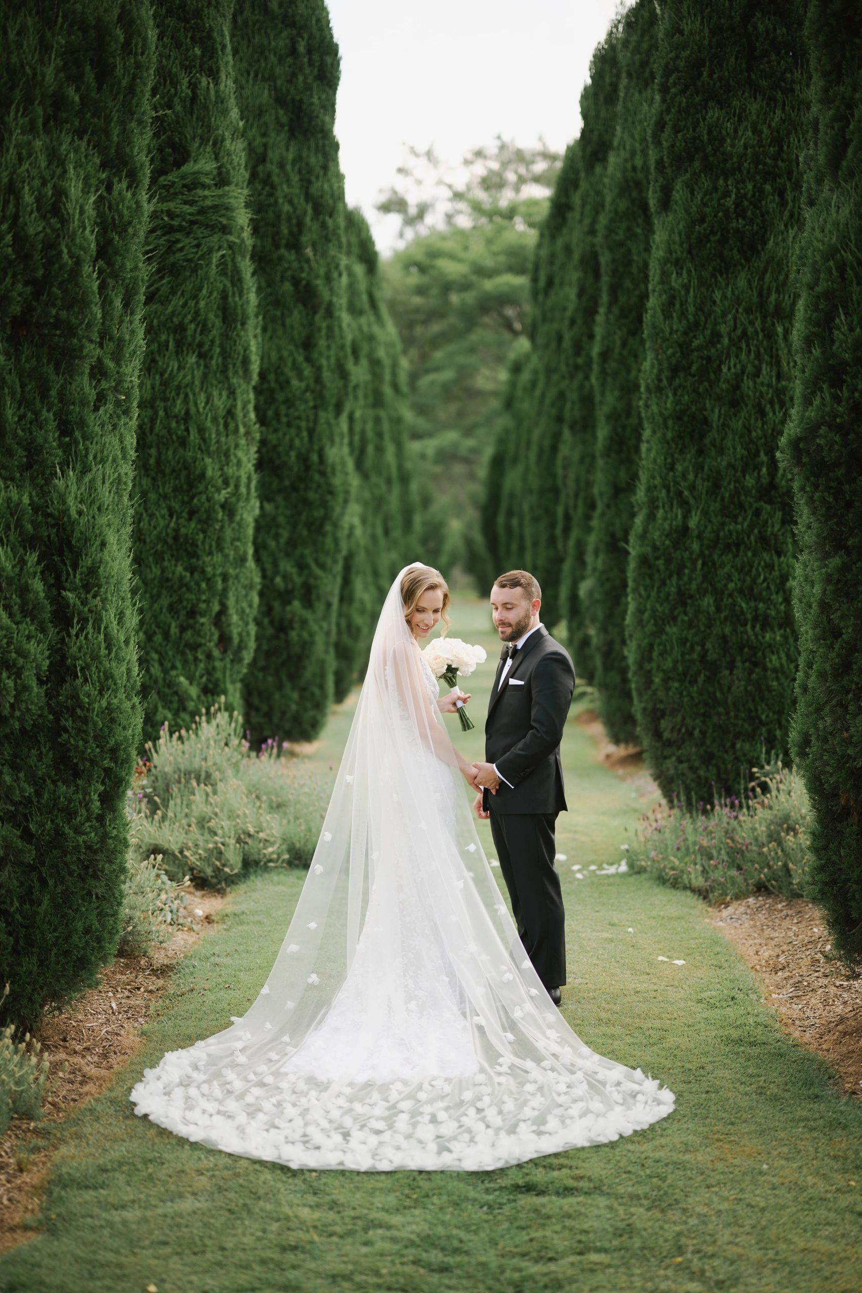 Married couple in the forest. Bride with beautiful veil and gown holding her bouquet. 