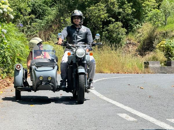 Two people riding a motorcycle with a sidecar on a sunny road in Portugal.