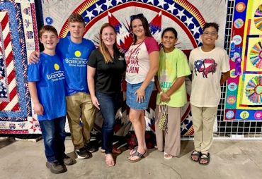 Group of smiling people standing in front of colorful quilts.