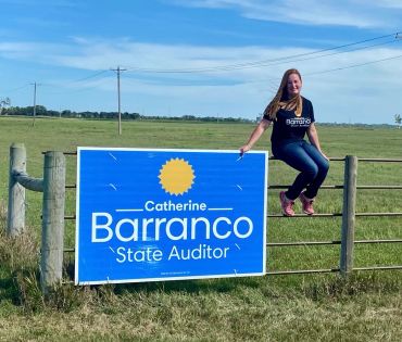 Catherine Barranco sitting on a fence with her campaign sign.