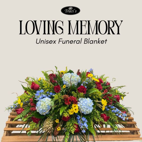 Floral funeral arrangement with red, blue, and yellow flowers on wooden base.