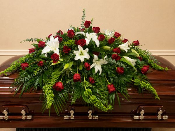 Floral arrangement with red roses and white lilies on a wooden coffin.