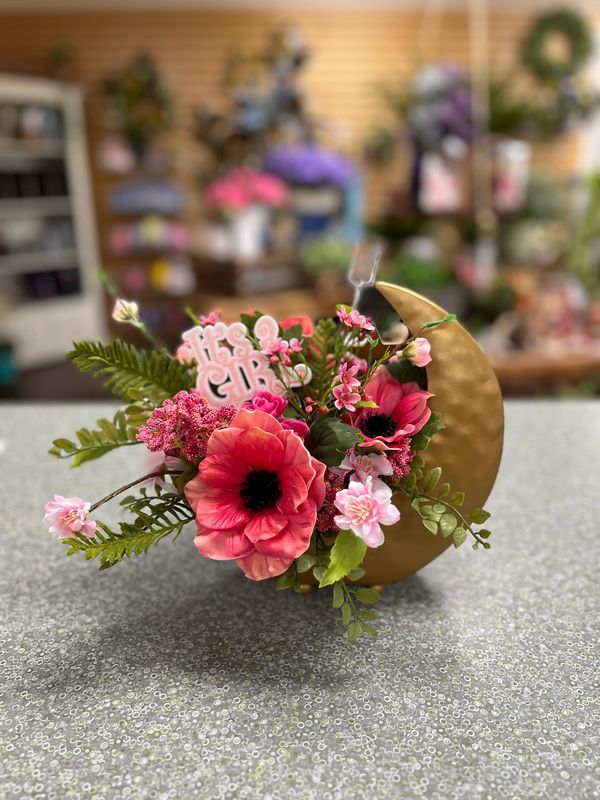 Floral arrangement with pink flowers and greenery in a gold crescent moon vase.
