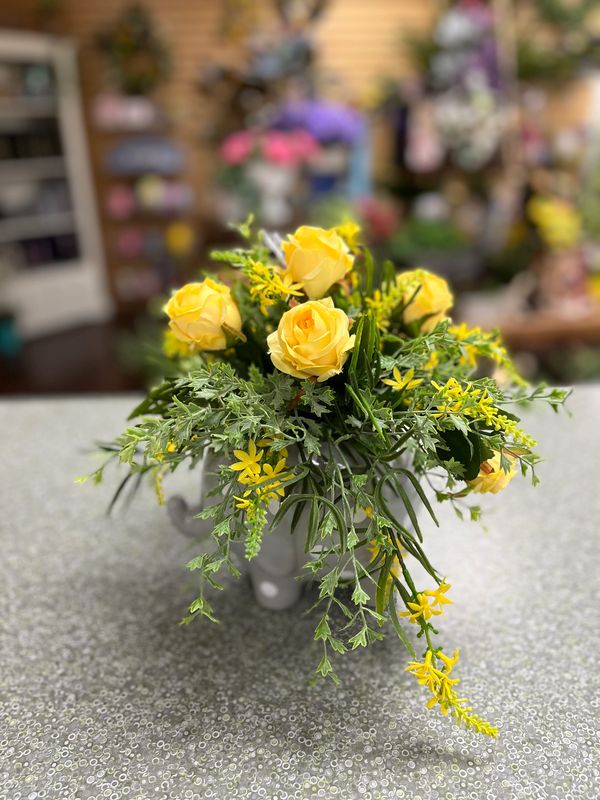 A bouquet of yellow roses and greenery on a patterned table.