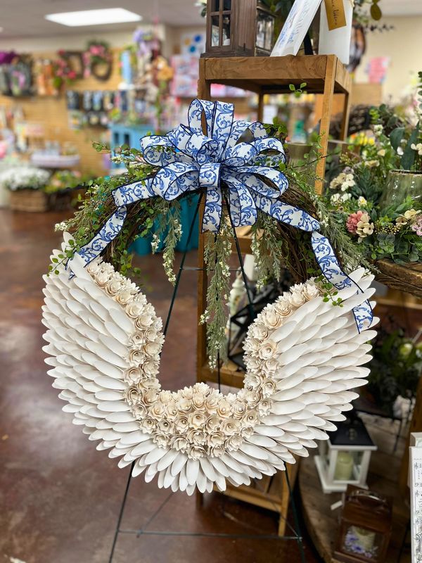 Elegant white floral wreath with a blue patterned bow, displayed in a shop.