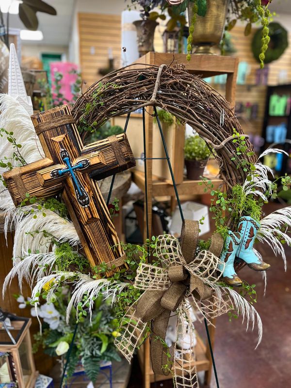 Rustic wreath with cross, blue boots, and burlap bow on display.