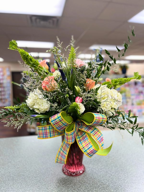 Colorful floral arrangement with a plaid ribbon in a red vase.
