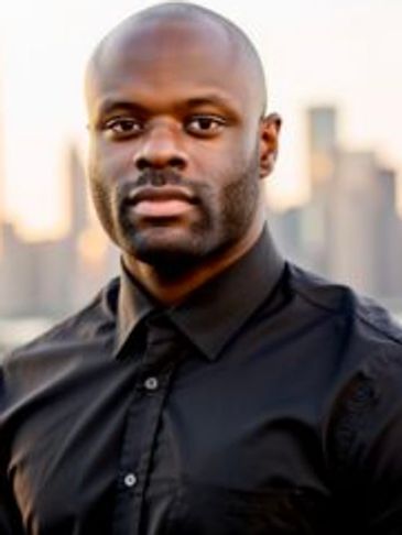 Confident man in black shirt with city skyline at sunset.