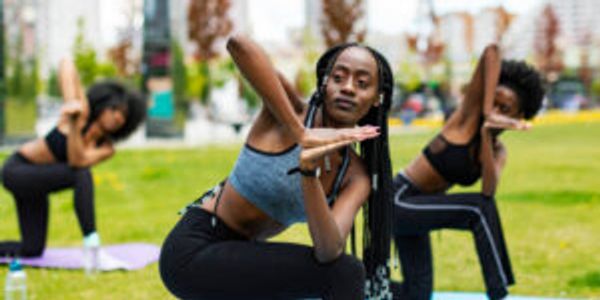 Three women practicing yoga outdoors on mats in a park.