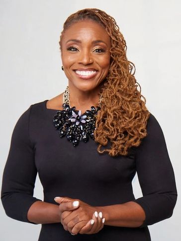 Confident woman with curly hair in a black dress and statement necklace smiling warmly.