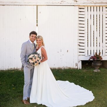 Newlywed couple posing happily outside by a rustic white barn.