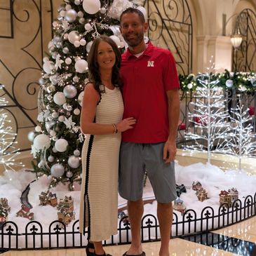 Couple posing in front of a decorated Christmas tree with festive lights.