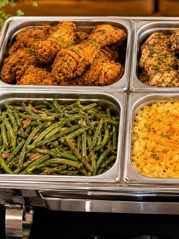 Buffet trays with fried chicken, grilled chicken, green beans, and macaroni and cheese.