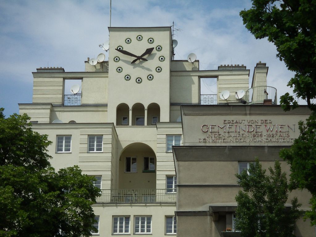 Historic white building in Vienna with a large clock and German inscription.