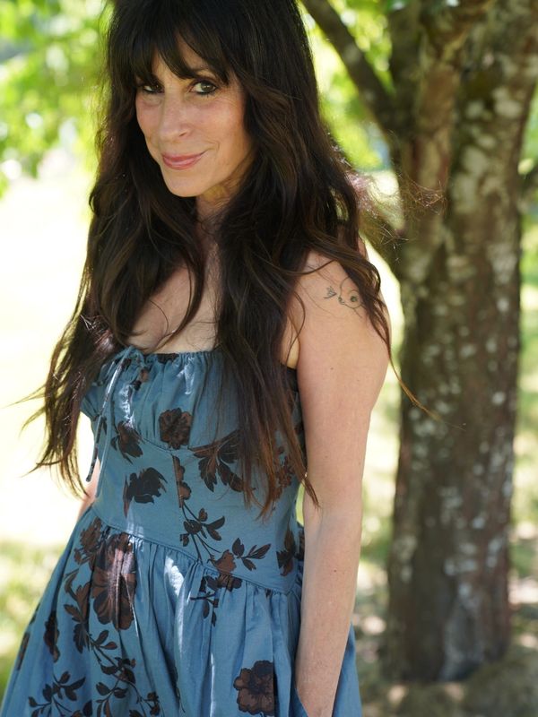 Woman with long dark hair in a floral dress outdoors.