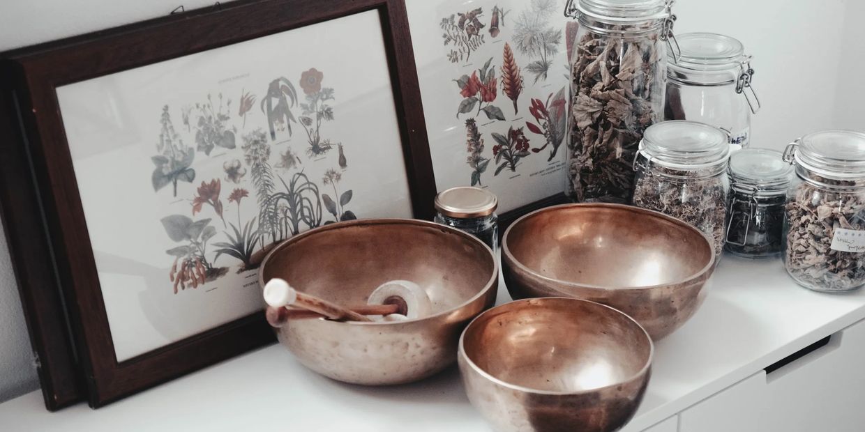 Three copper bowls on a white shelf, with botanical prints and glass jars of dried herbs