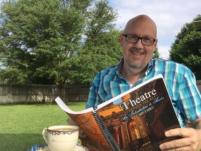 Dr Daryl R Worley sitting outdoors holding a Theatre book next to china coffee cup