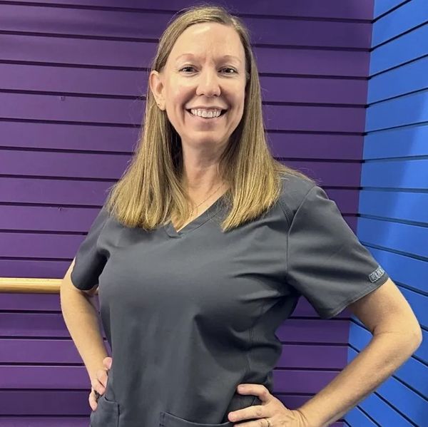 Smiling woman in gray scrubs against a purple and blue wall.