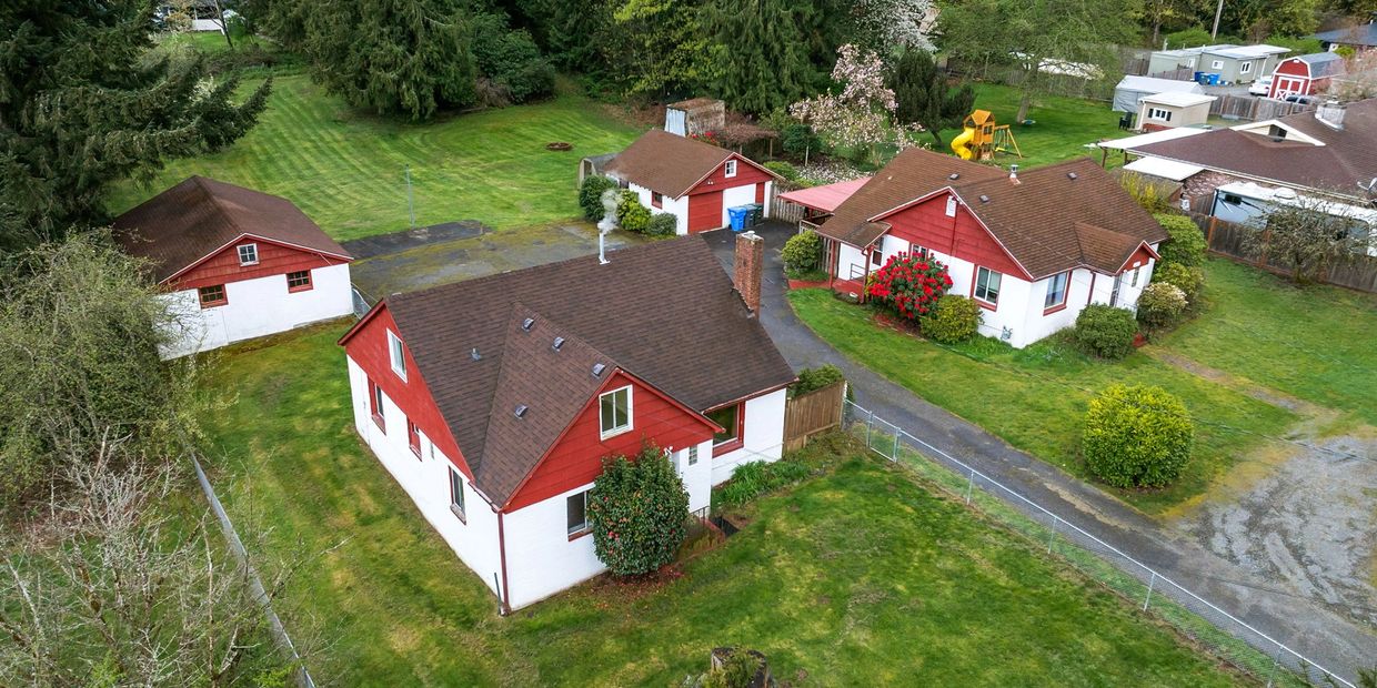 Aerial view of two red and white houses with brown roofs surrounded by green lawns.