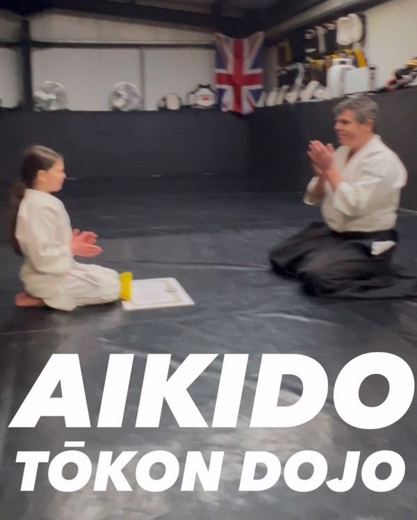 Aikido training session at Tōkon Dojo with instructor and student kneeling and clapping.
