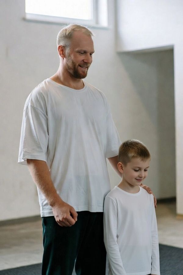 A man and a boy share a tender moment indoors, both wearing white shirts.