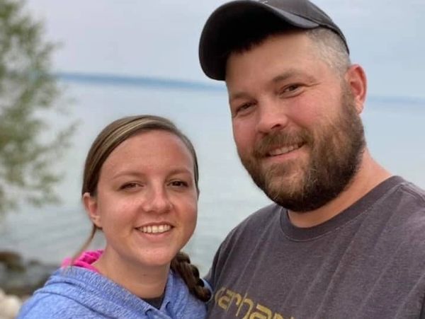 Smiling couple posing near a calm lake on a cloudy day.