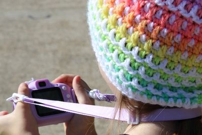Photograph of a child holding a camera a wearing a colorful crocheted hat. 