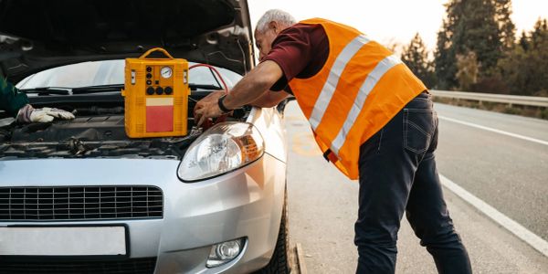 Man in reflective vest fixing a car engine on the roadside.