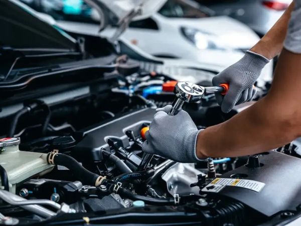 A mechanic wearing gloves repairs a car engine using a socket wrench.