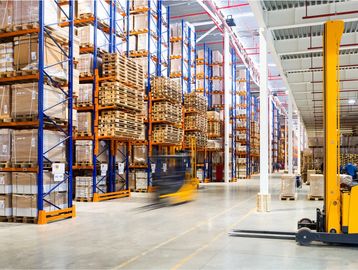 Busy warehouse with tall shelving and forklifts in motion.