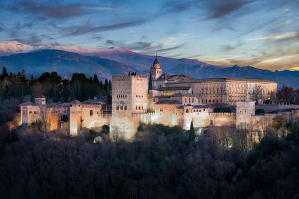 The Alhambra palace illuminated at dusk with mountains in the background.