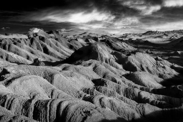 Black and white photo of rugged, eroded hills under a cloudy sky.