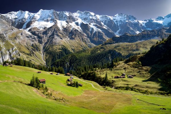 Snow-capped mountains overlooking a green valley with scattered houses.