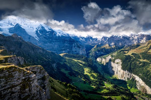 Snow-capped mountains overlooking the lush Lauterbrunnen valley of Switzerland under a cloudy sky.