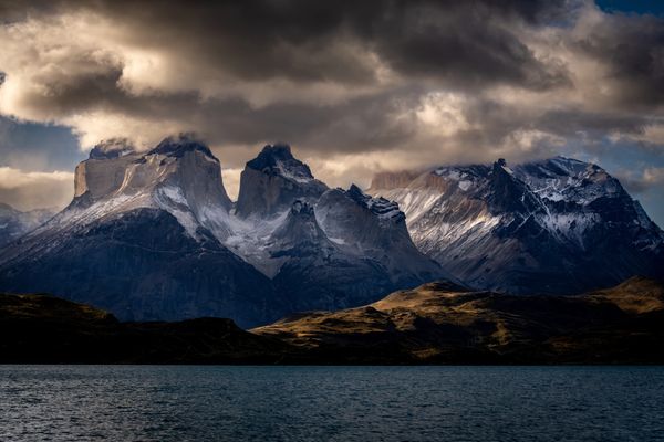 Dramatic mountain peaks under dark, swirling clouds with sunlight casting shadows.