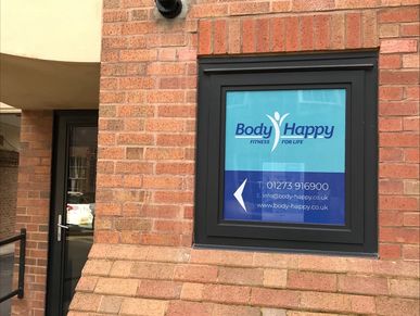 Sign for Body Happy fitness center on a brick wall.
